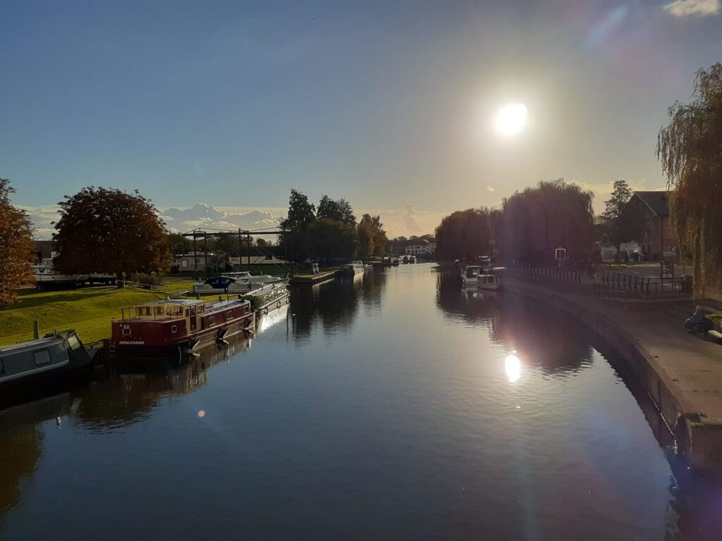 A river and a boat glistening in the backlight, in Ely, England