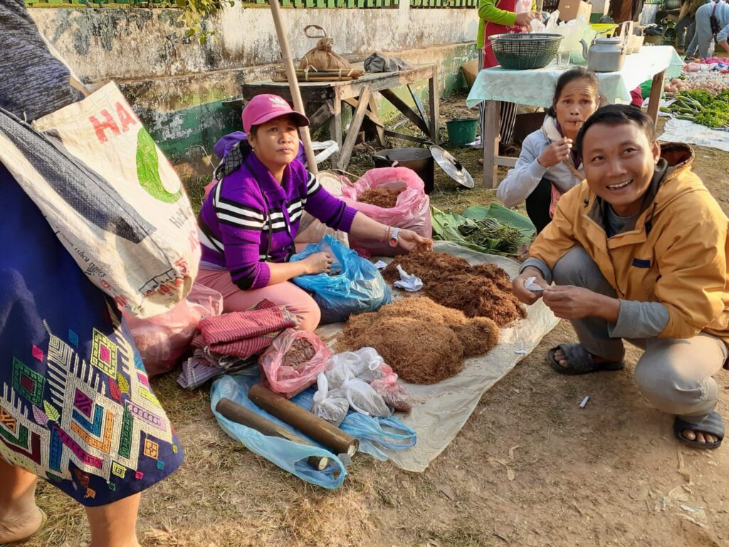 A tobacco leaf vendor and a customer trying it out in the morning market in Muang Ngoy
